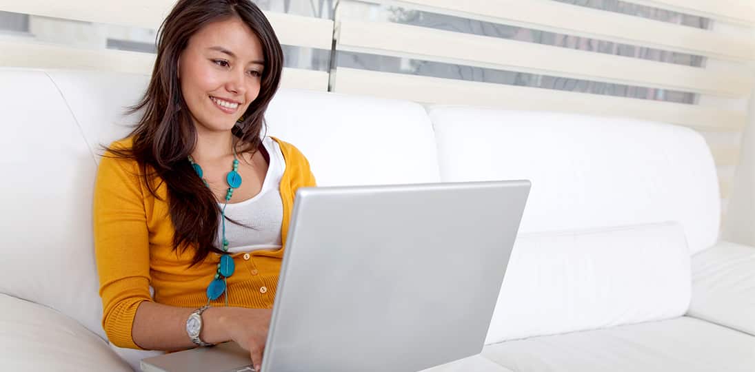 woman in yellow shirt sitting on white couch with laptop open for software updates
