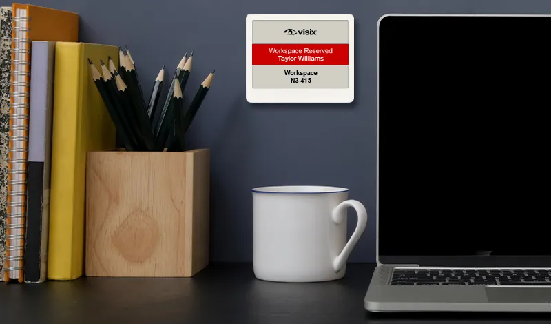 image of small epaper desk sign mounted on the wall next to a laptop and pencil holder, above a coffee mug