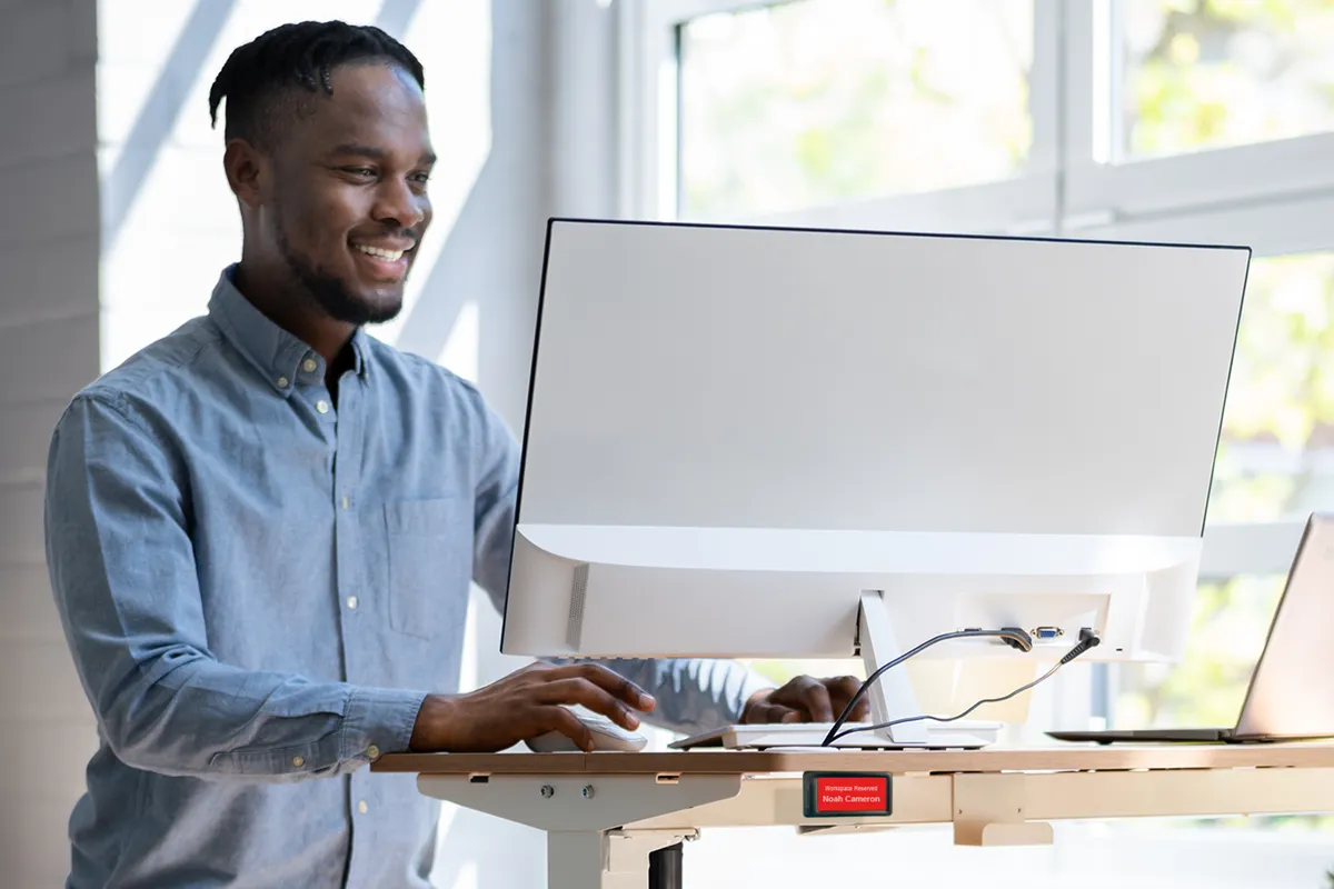 photo of man at standing desk in office with epaper desk sign showing hotdesking reservation