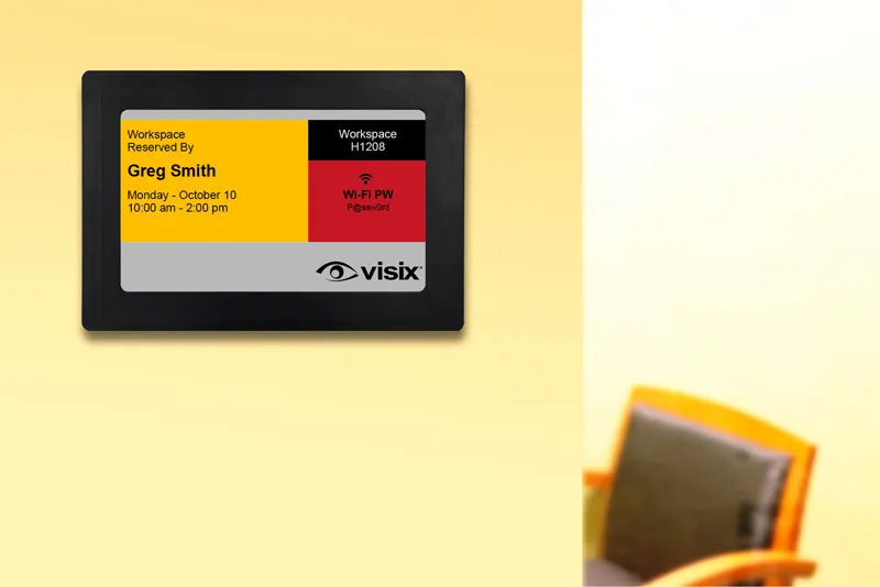 ePaper wireless sign mounted on wall outside hybrid office showing office hoteling reservation in black, red and yellow ink.
