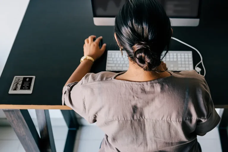 ePaper desk sign with desk reservation details in black block on graphic photo background of justice statue mounted on desk with woman working on computer