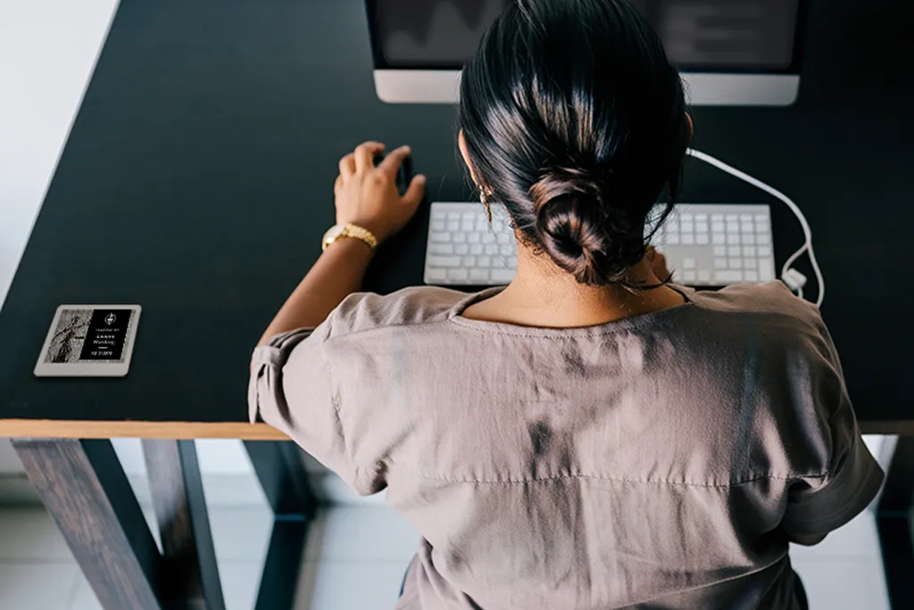 ePaper desk sign with desk reservation details in black block on graphic photo background of justice statue mounted on desk with woman working on computer