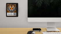 ePaper desk sign with desk reservation QR code in white block with tiger head graphic mounted on wall behind desk with keyboard, mouse and monitor