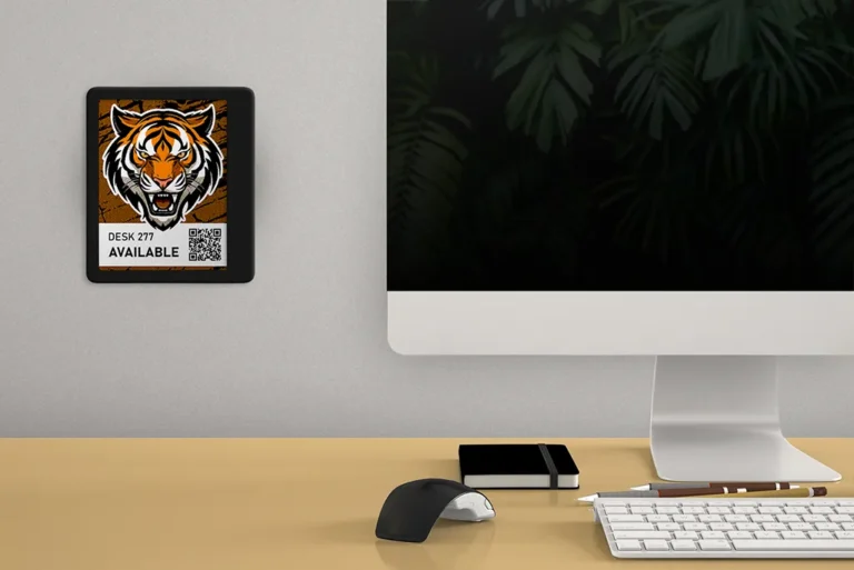 ePaper desk sign with desk reservation QR code in white block with tiger head graphic mounted on wall behind desk with keyboard, mouse and monitor