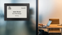 ePaper sign mounted on glass outside of shared office showing digital nameplate with reservation data