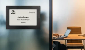 ePaper sign mounted on glass outside of shared office showing digital nameplate with reservation data