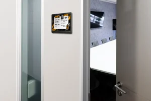 ePaper room sign with black and yellow hornets graphics mounted on wall outside meeting room