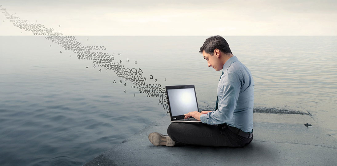 man sitting on beach water working on laptop; get tips for successful digital signage configuration