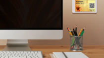 ePaper desk sign with plant background graphic and QR tag to make desk reservations mounted on wall beside monitor and above cup of pencils