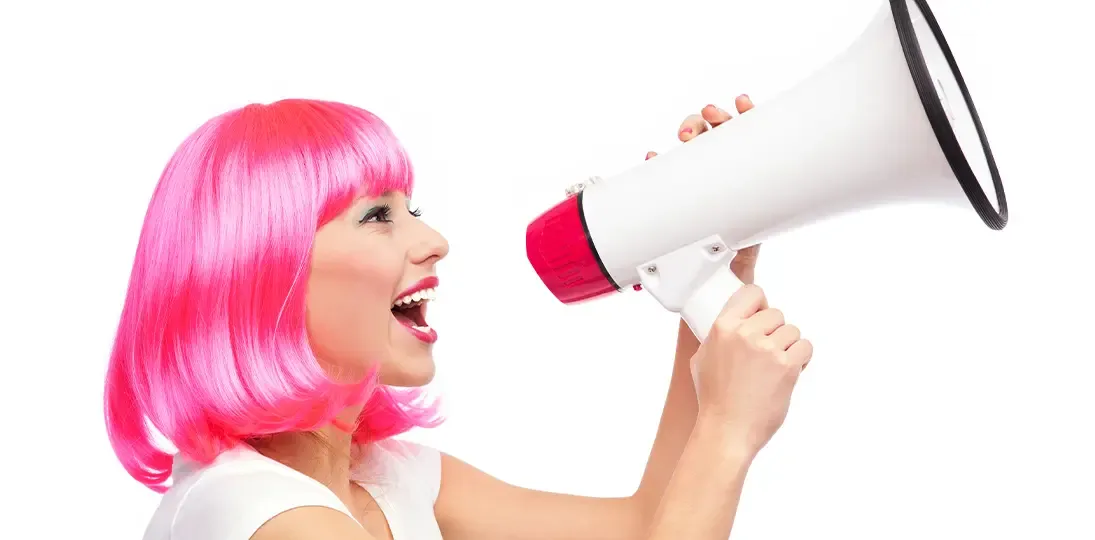 photo of woman with pink hair smiling and calling people to action using a megaphone