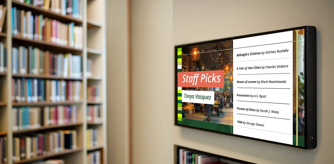 photo of digital signage display on library wall showing staff book recommendations next to bookshelves